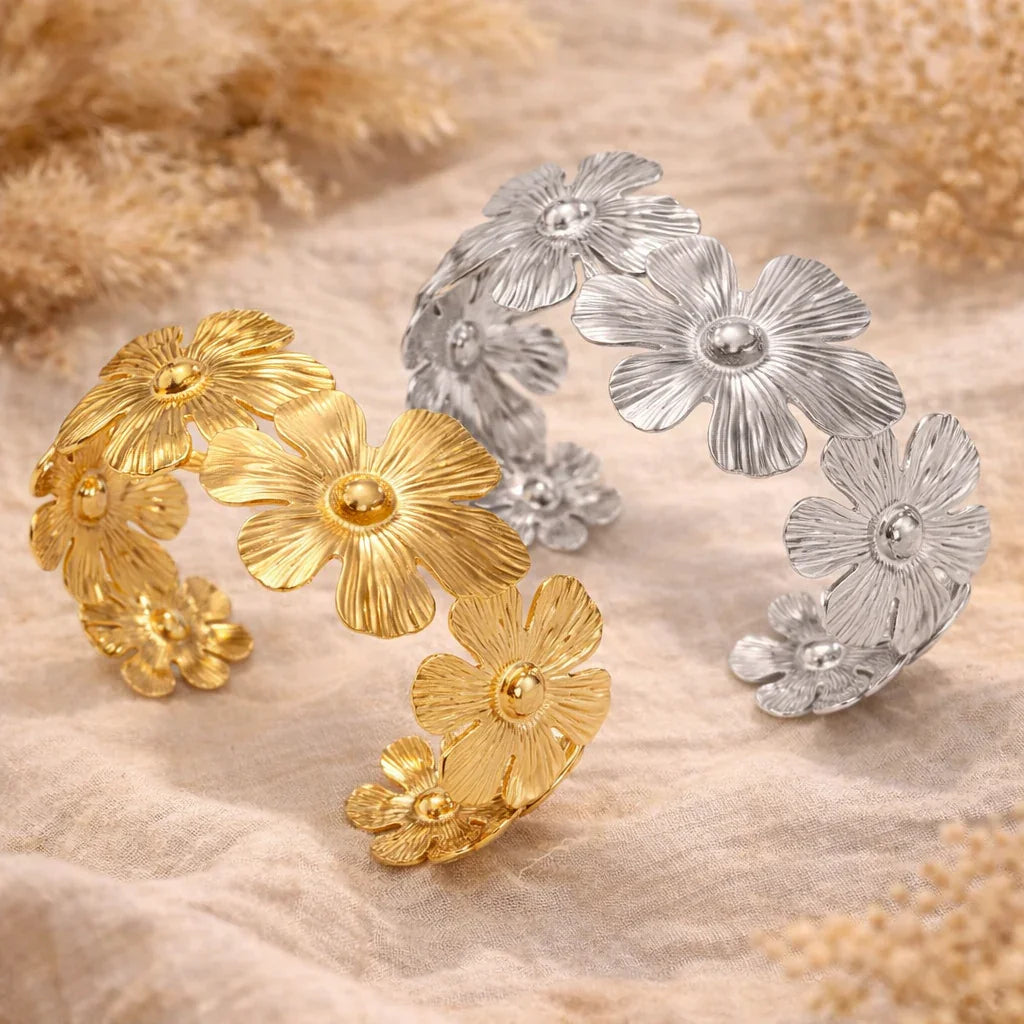 Bracelets bohème ouverts en acier inoxydable doré et argenté, motif fleurs, posés sur tissu beige.