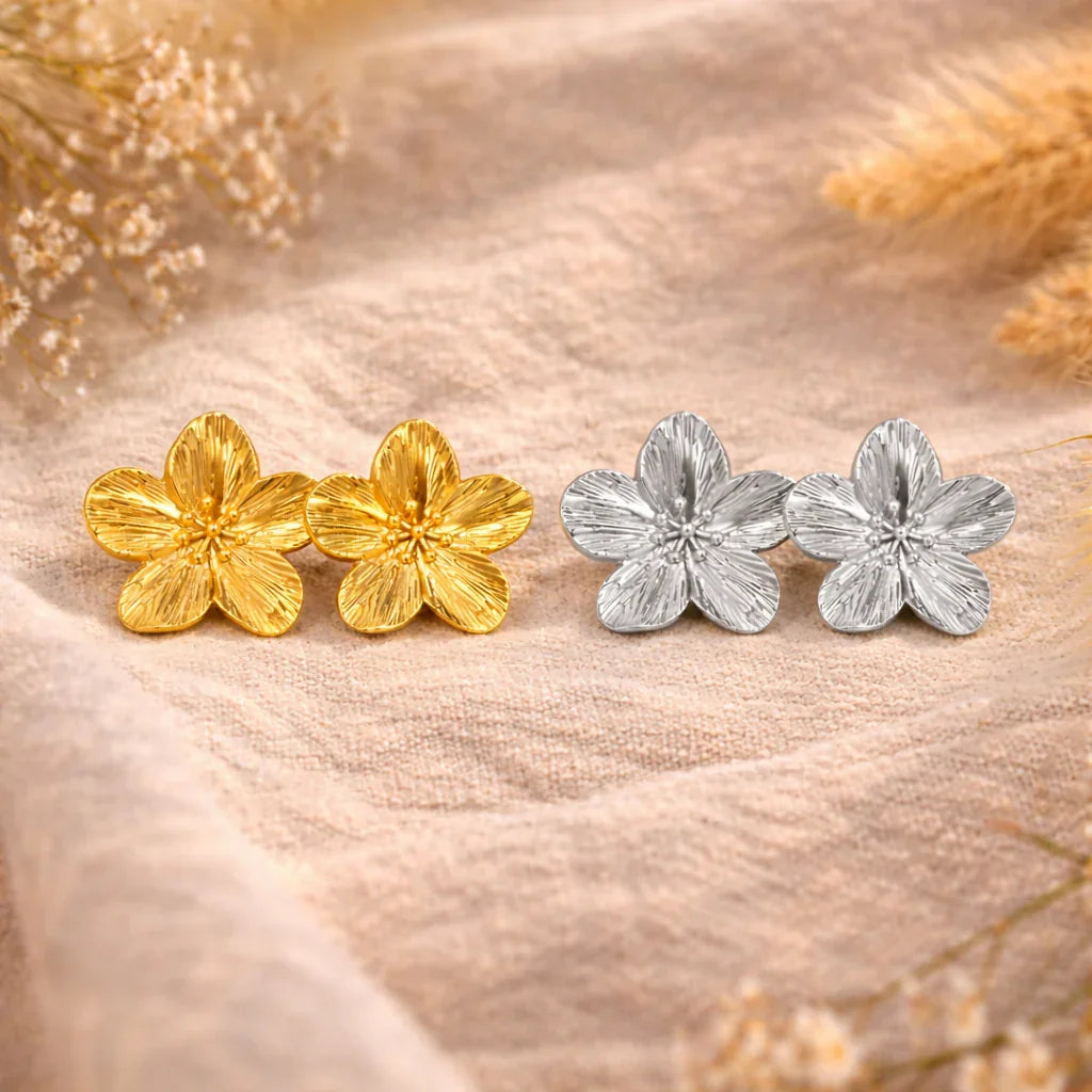 Boucles d’oreilles bohème en forme de trèfle, acier inoxydable doré et argenté, posées sur tissu beige.
