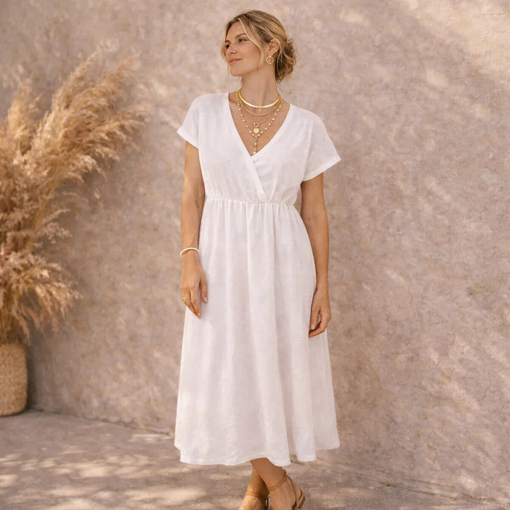 Femme portant un collier multi-rangs doré style bohème, robe blanche, décor naturel.