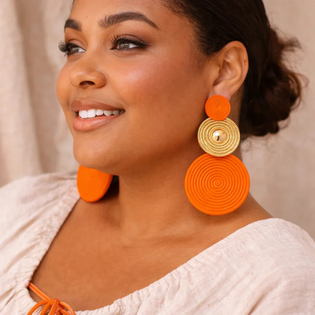 Femme portant de grandes boucles d’oreilles bohème orange avec détails dorés, style élégant.